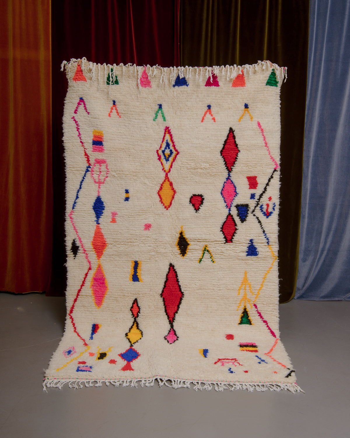Azilal rug held in front of velvet curtains. 