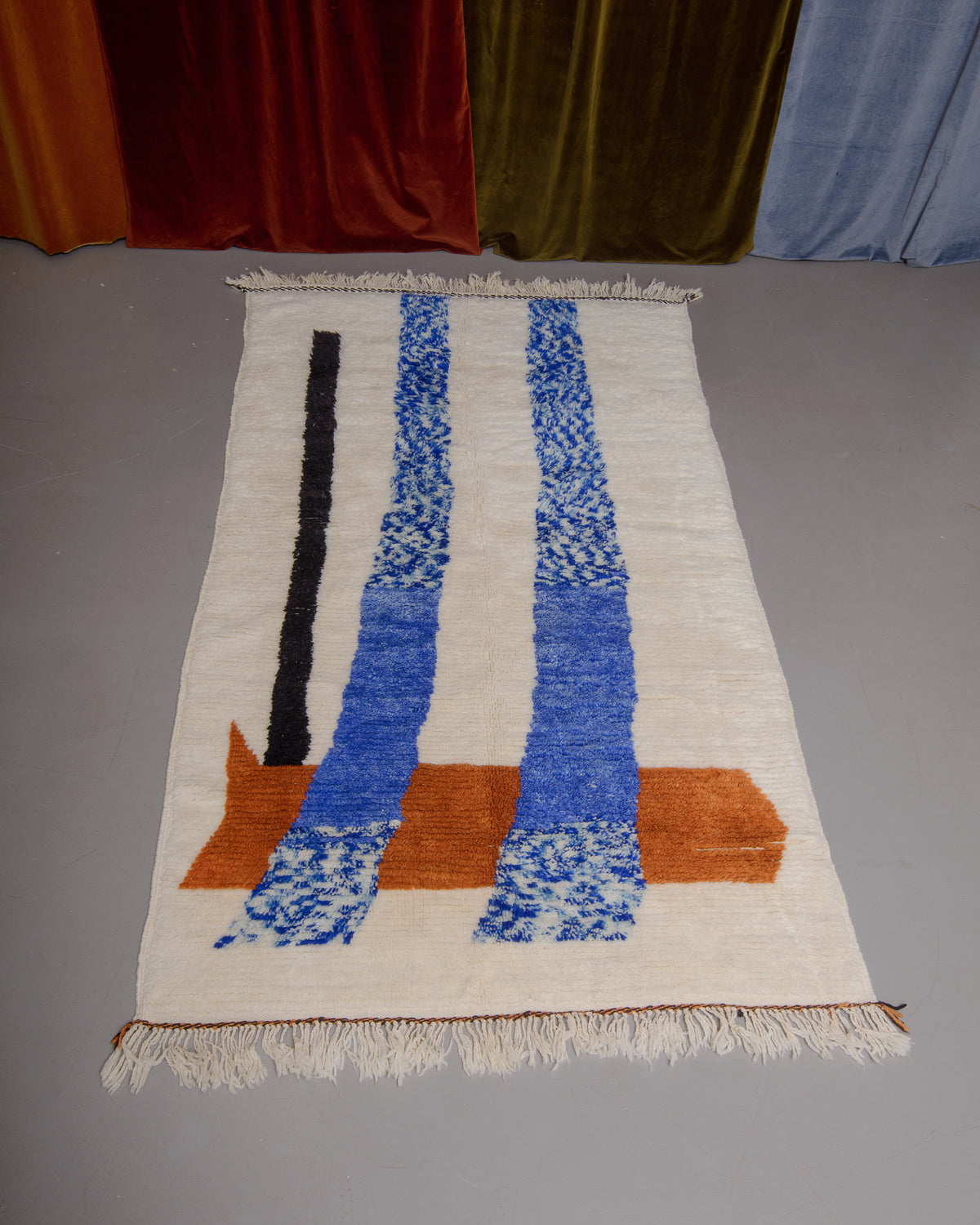 Azilal rug featuring colourful design on a grey floor in front of curtains.