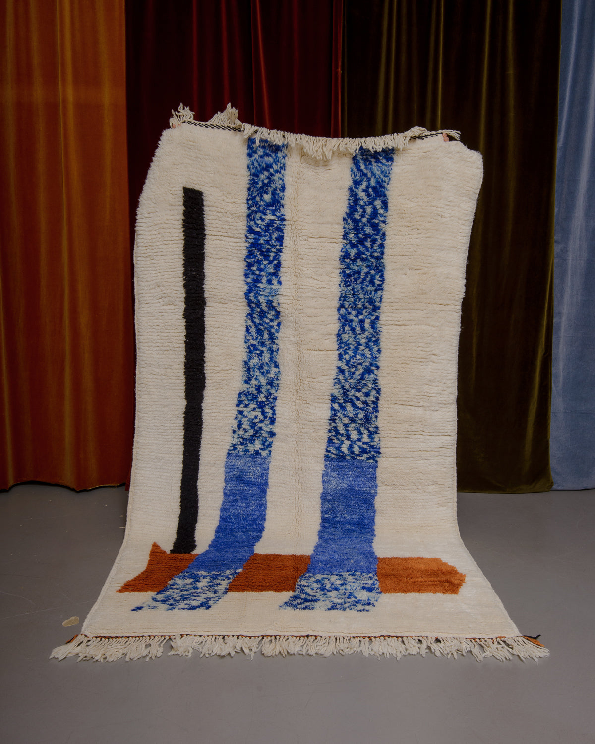 Azilal rug held in front of velvet curtains. 