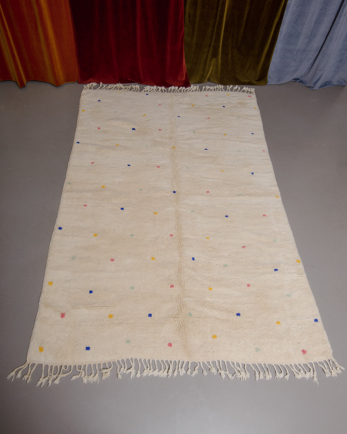 Cream wool rug with colourful polka dots on grey floor. 
