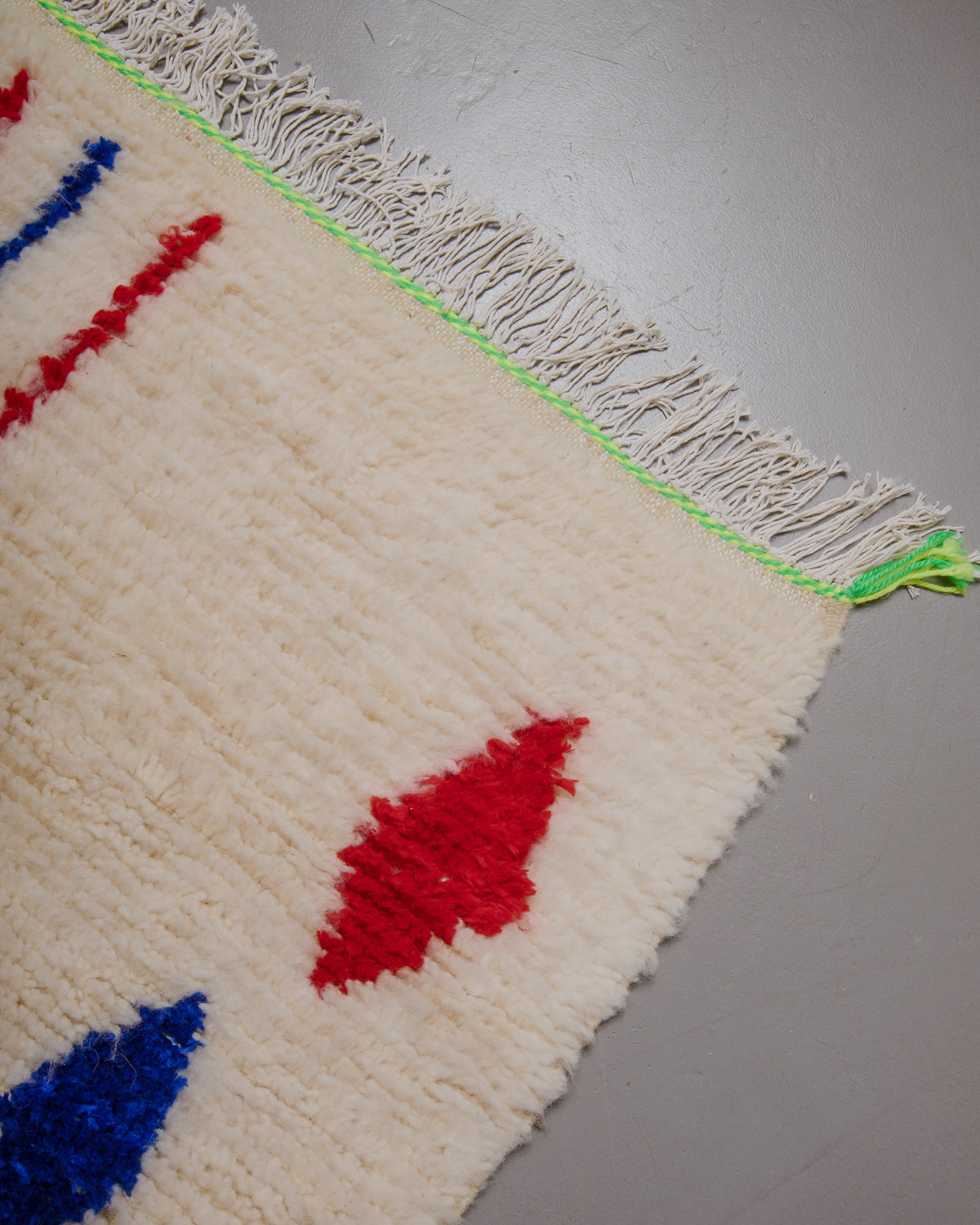 Corner of azilal rug with white cotton fringe and neon stitching across the end.