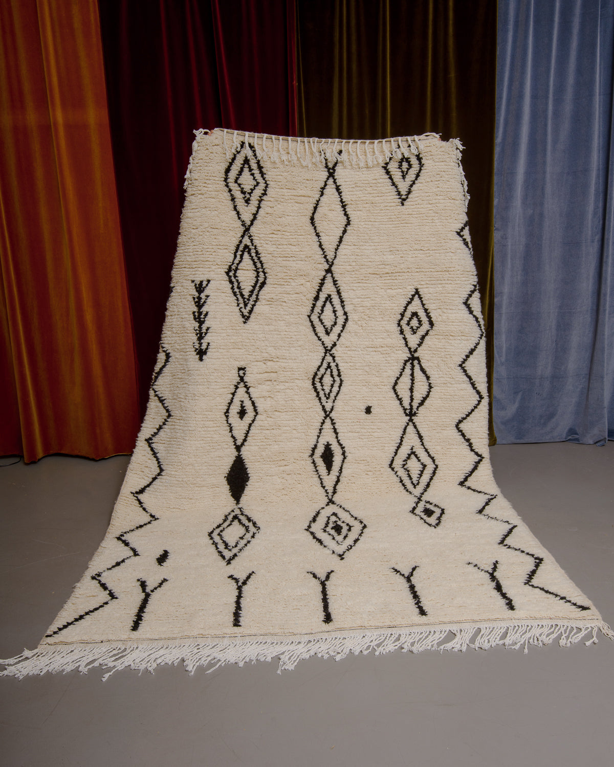 Azilal rug with abstract design in black being held up in front of a wall of velvet curtains.