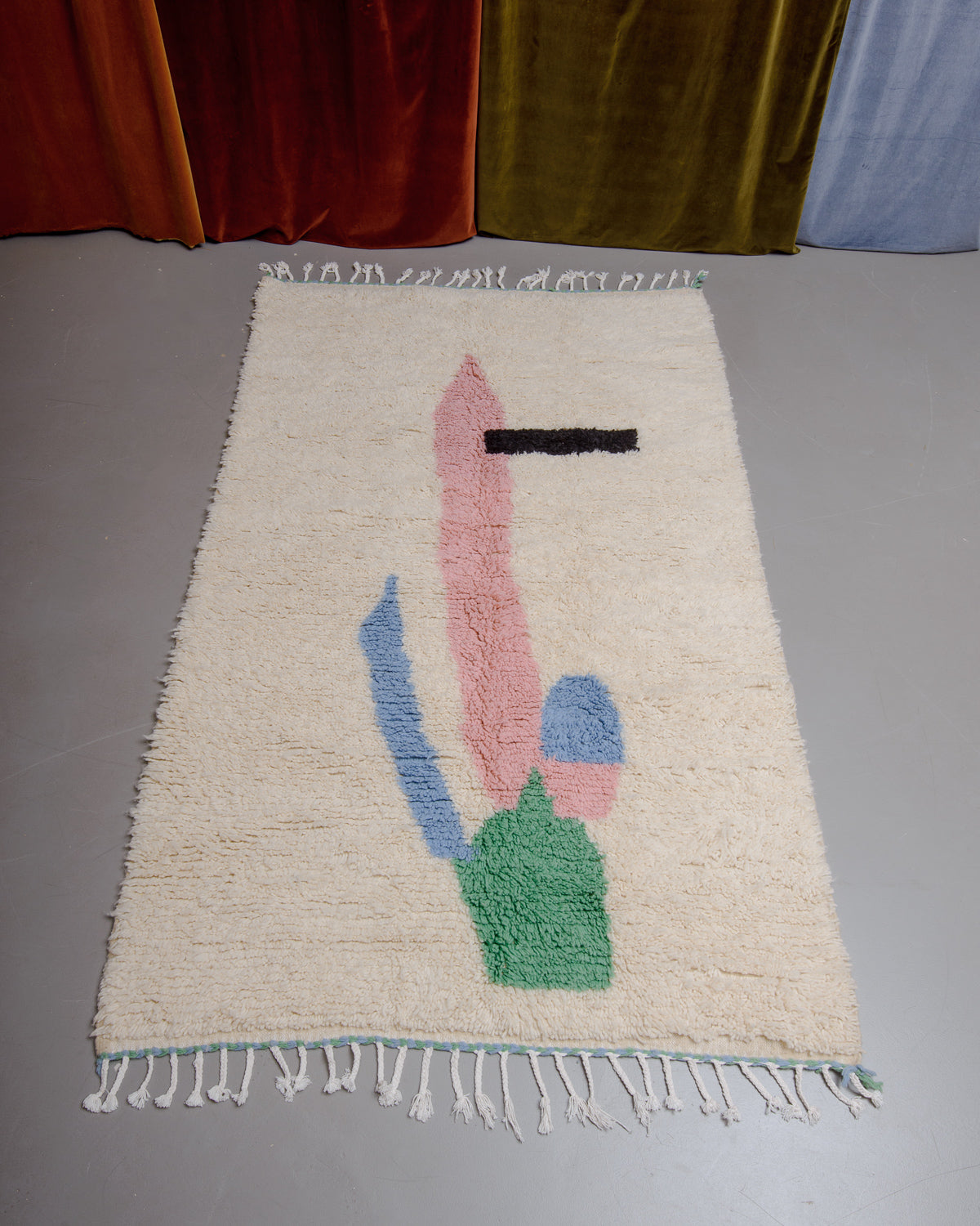 Azilal rug featuring colourful design on a grey floor in front of curtains.