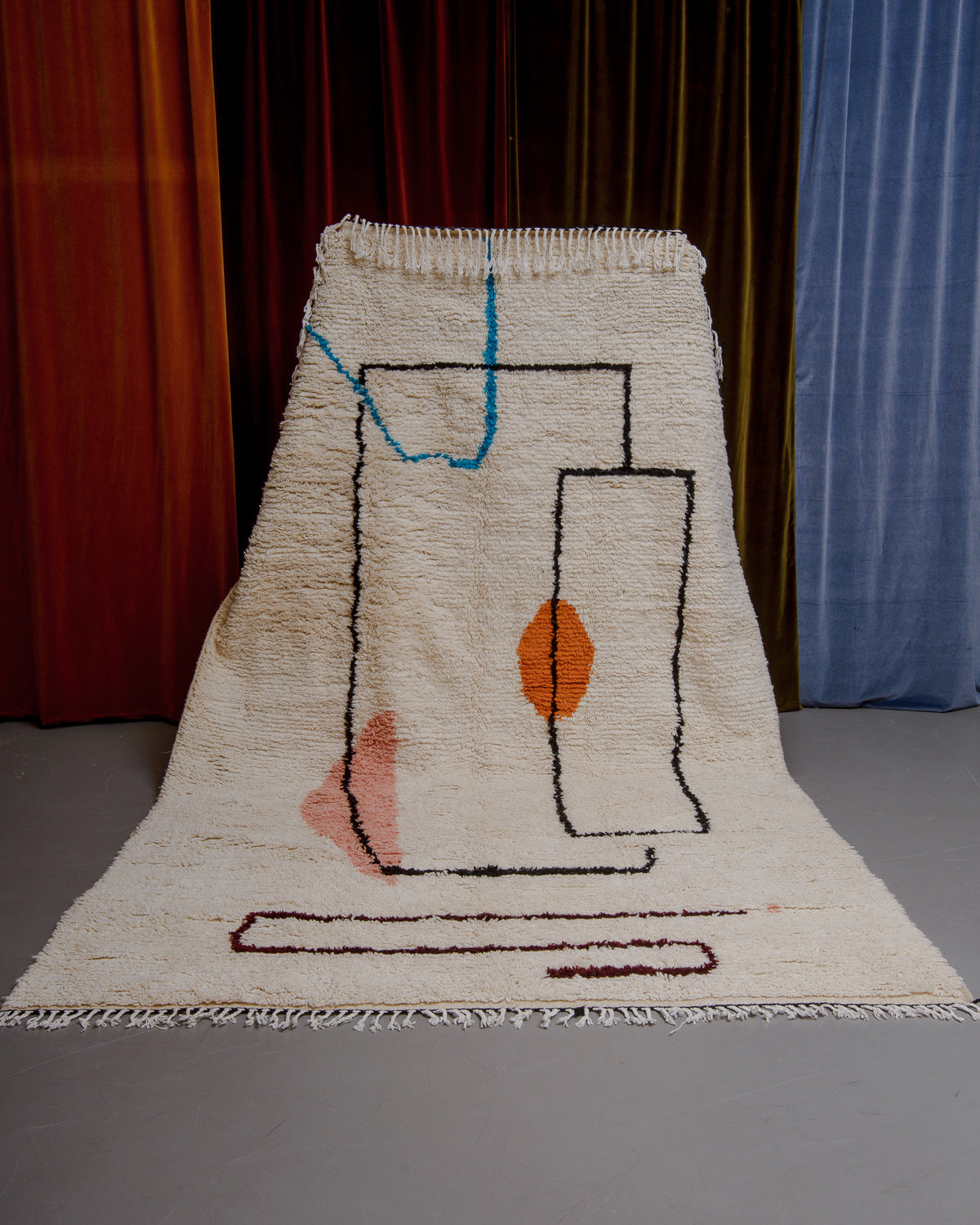 Azilal rug held in front of velvet curtains. 
