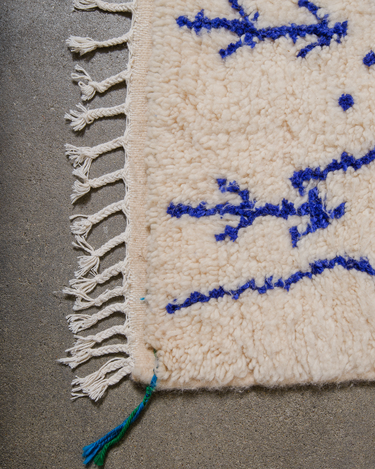 Edge of Azilal rug with blue and green corner tassels and white cotton tassels along the edge.