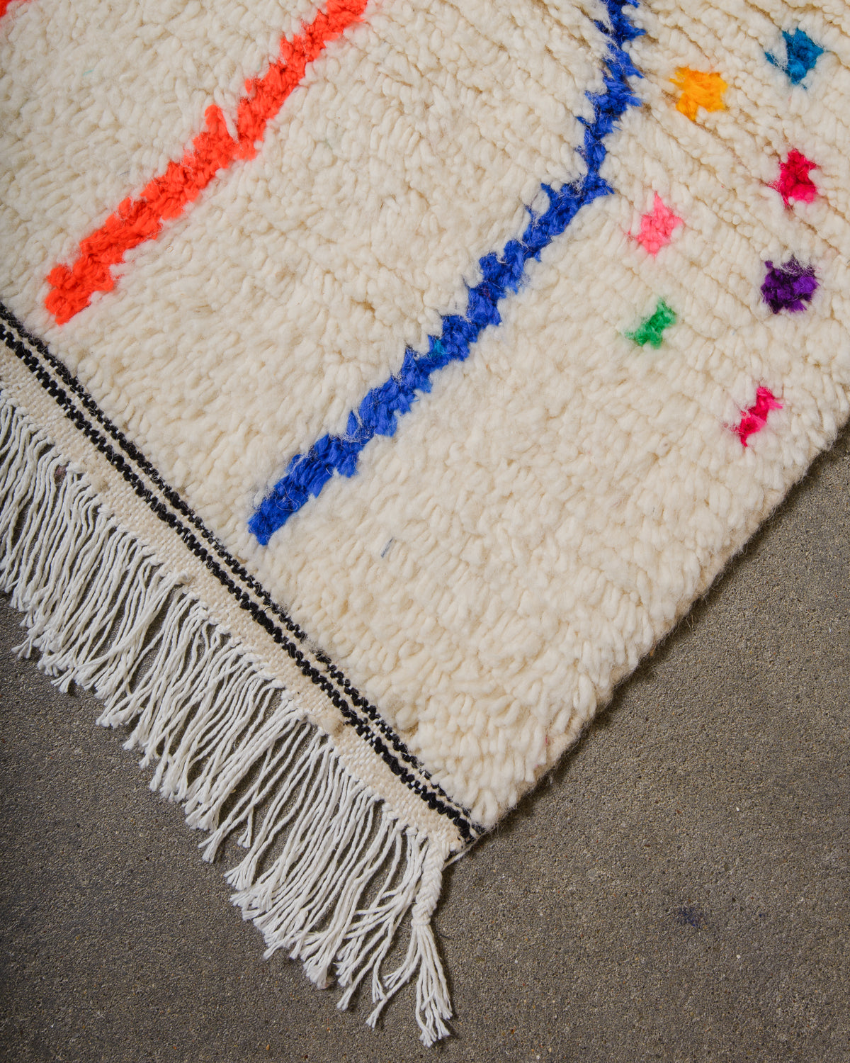 Edge of Azilal rug with black detail and white cotton tassels along the edge.
