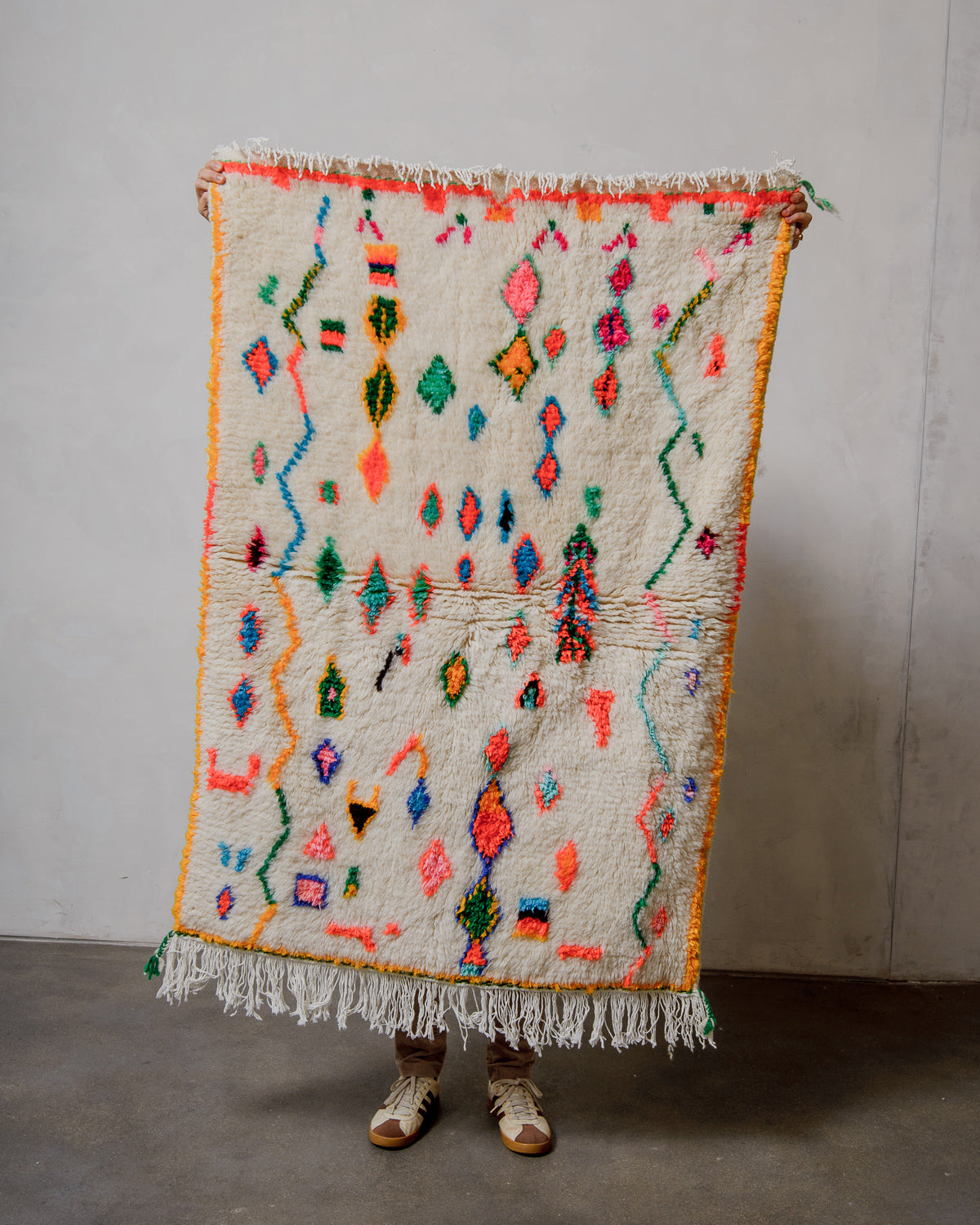 Person holding a colorful patterned rug against a plain background