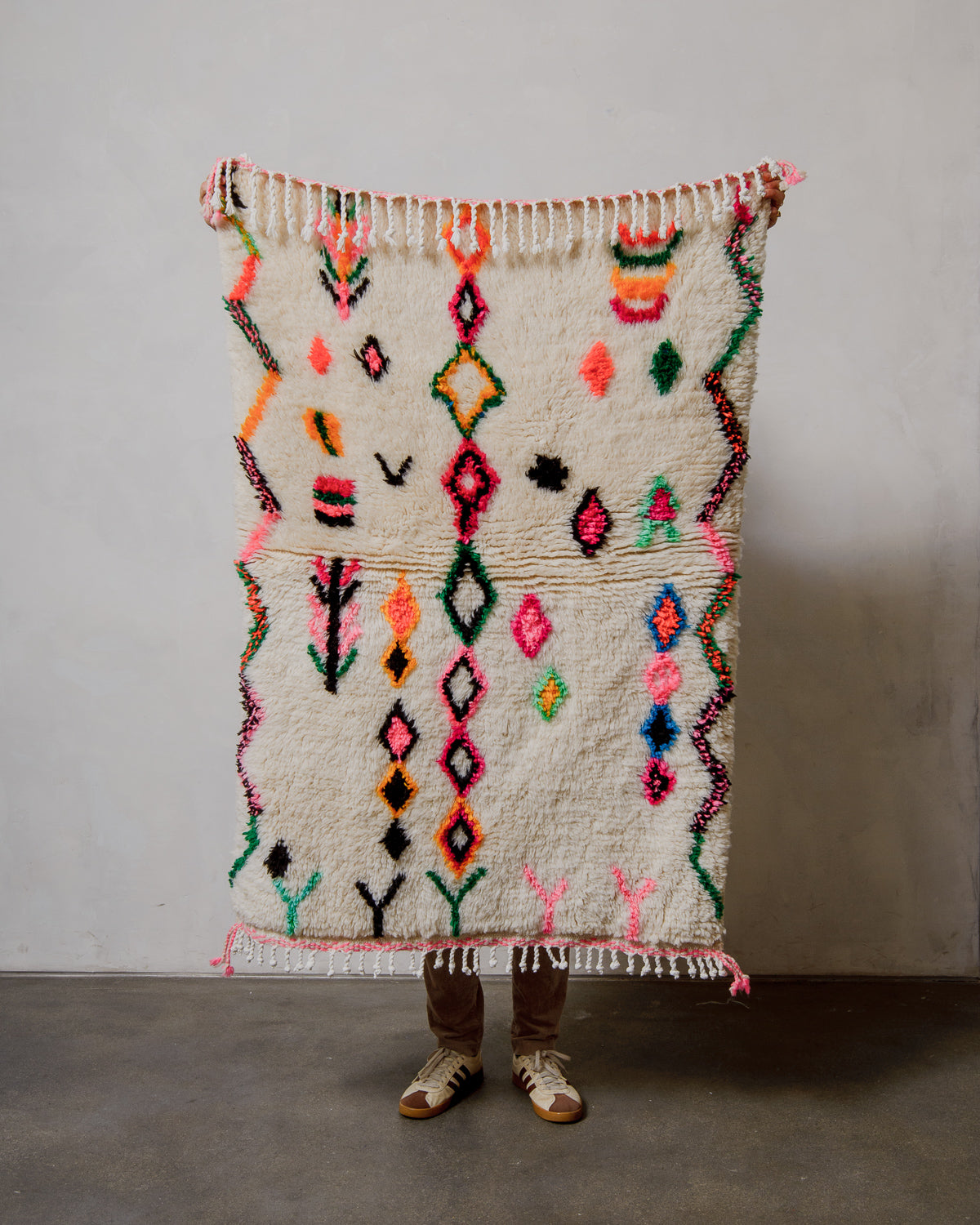 Person holding a colorful Berberlin Finest rug against a plain background