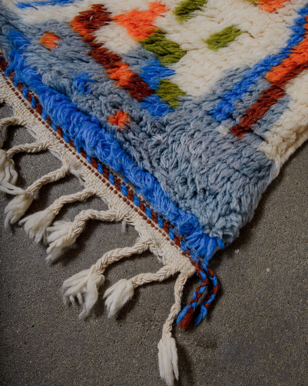 Corner of a colorful woven wool rug with tassels on a textured surface