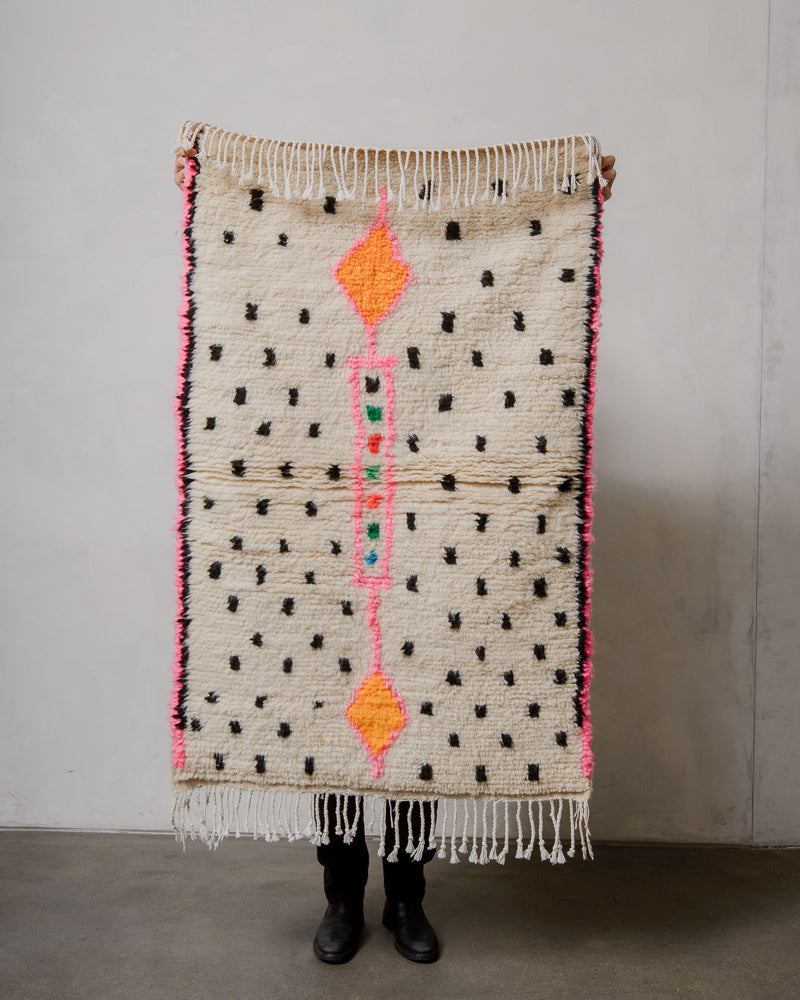 Azilal rug with black dot pattern held up by a person against a plain background