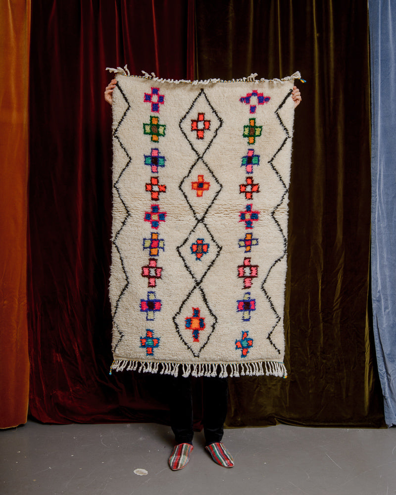 Berberlin Azilal rug with colourful motifs held in front of a velvet curtain.