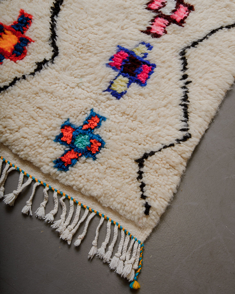 Corner of Berberlin Azilal rug with colourful motifs and white cotton tassels.