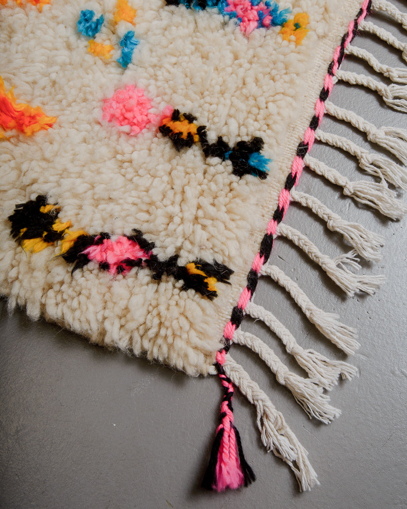 Corner of Berberlin Azilal rug with white cotton tassels and black and pink edge.