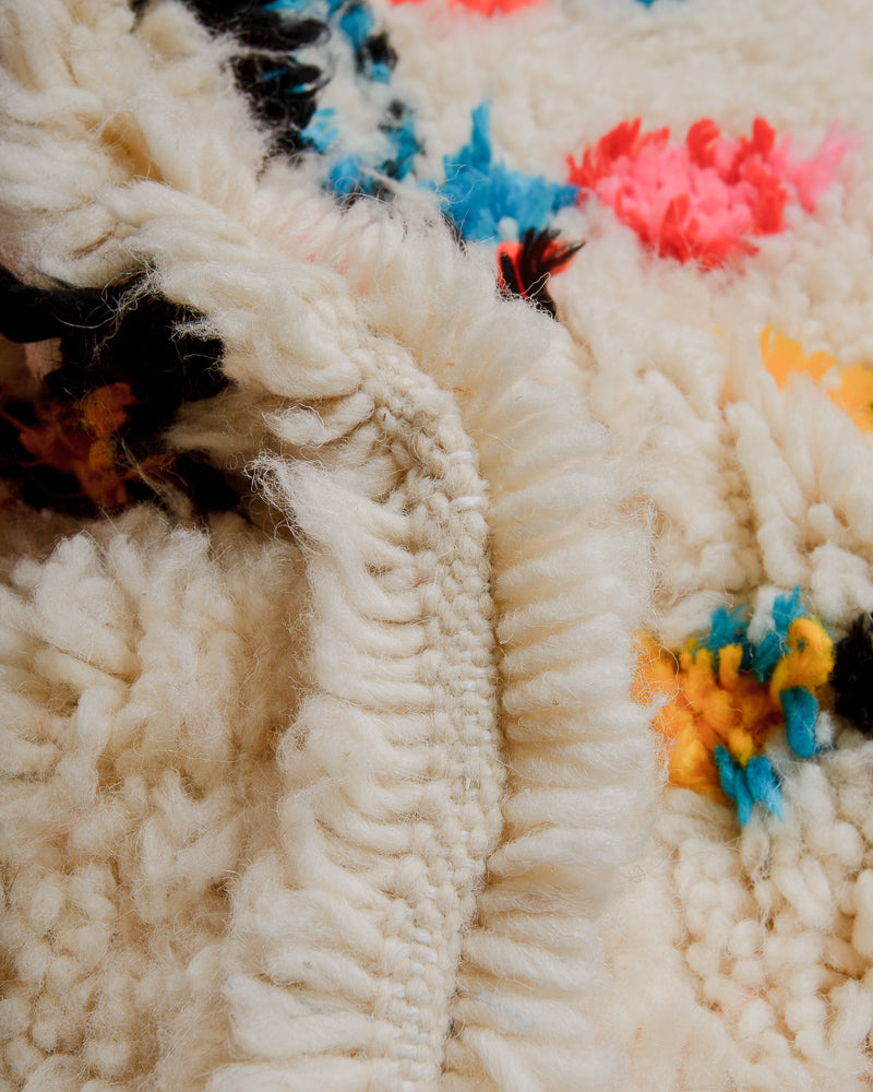 Close up of cream wool rug with colourful cotton details. 