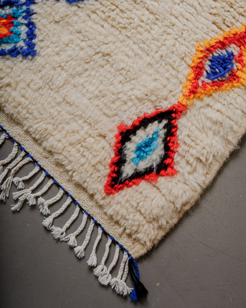 Corner of wool rug with cream wool and colourful cotton accents and white cotton tassels.
