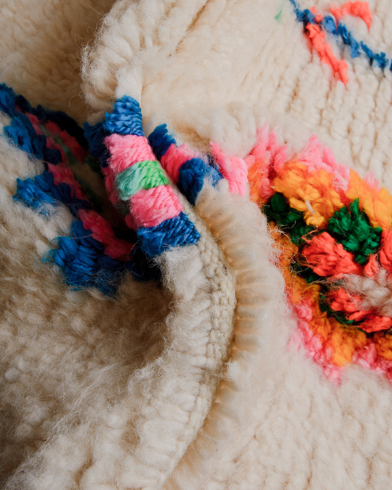 Close up of rug with cream wool and colourful cotton in green, blue, yellow and pink