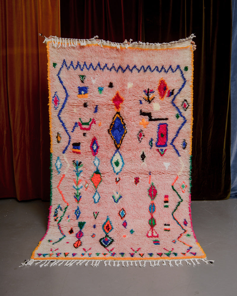 Berberlin Azilal rug with pink wool and colourful cotton being held up in front of velvet curtains.