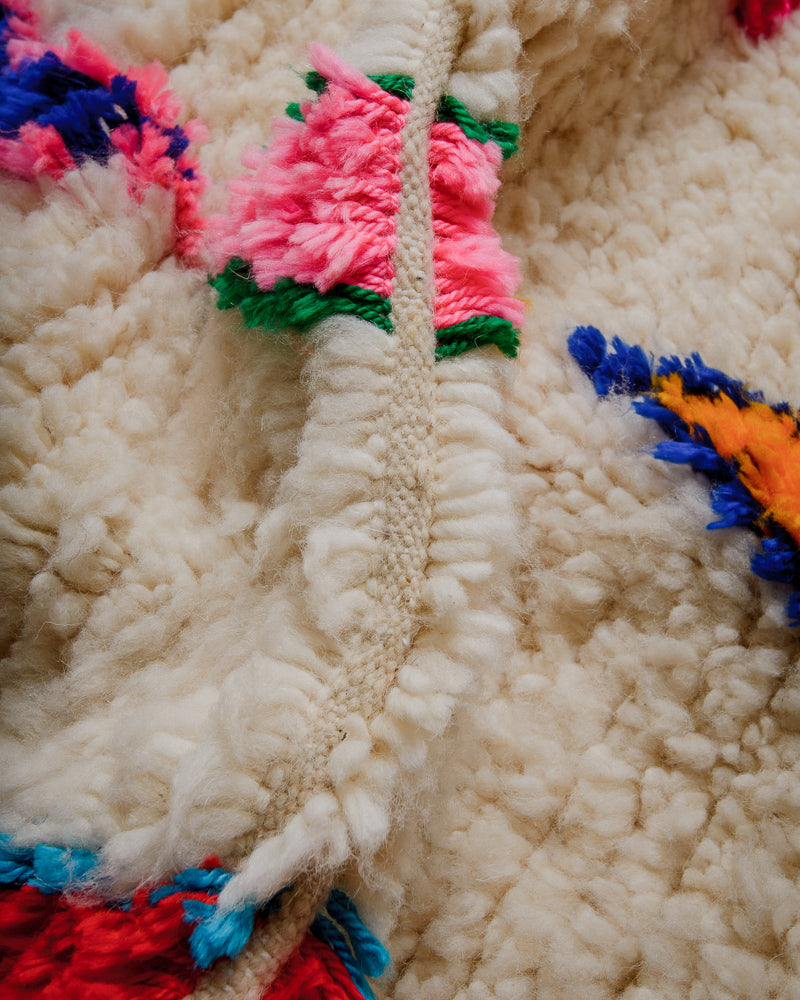 Close up of wool rug with colourful cotton in  pink, green, orange, and blue.