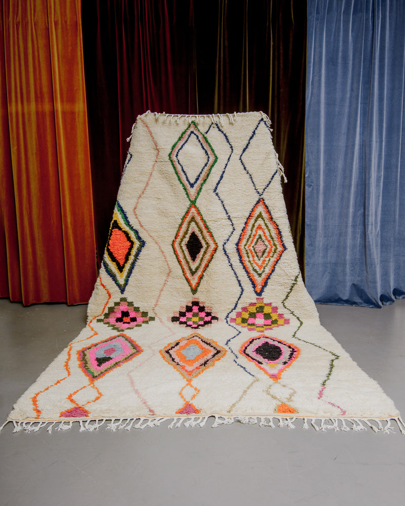 Colourful azilal rug held in front of velvet curtains. 