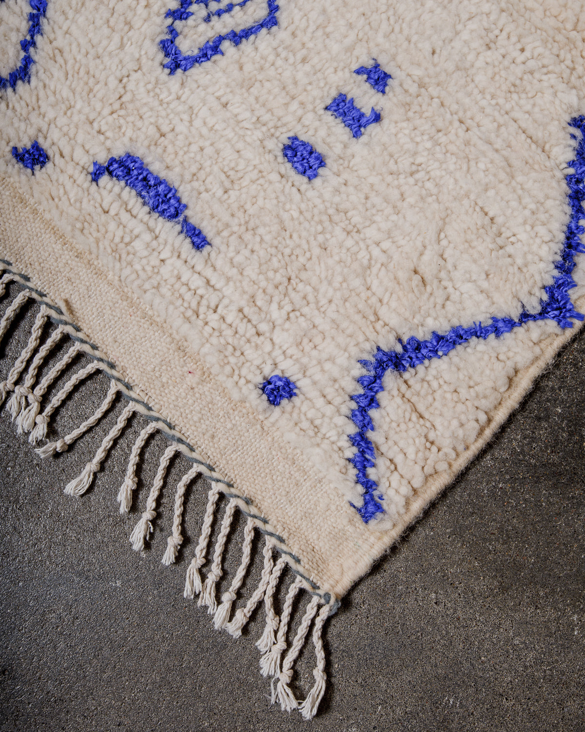 Corner of Azilal rug with a tightly woven edge and white cotton tassels along the end.