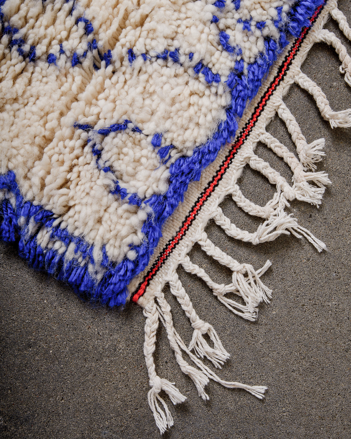 Corner of Azilal rug with a tightly woven edge and white cotton tassels along the end.