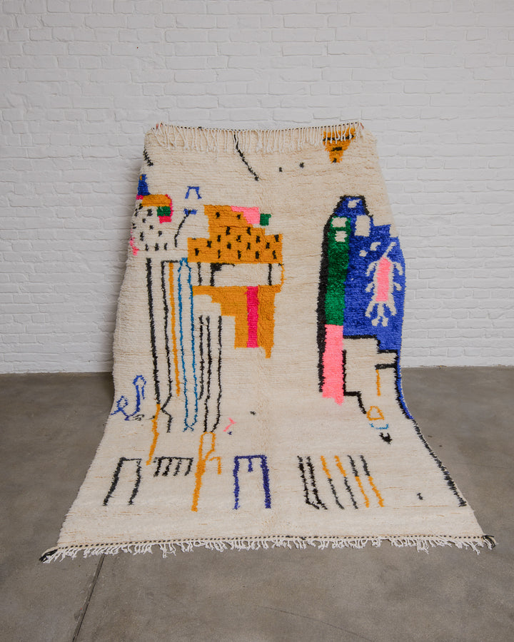 Cream azilal rug with modern, abstract design being held up in front of white brick wall. 