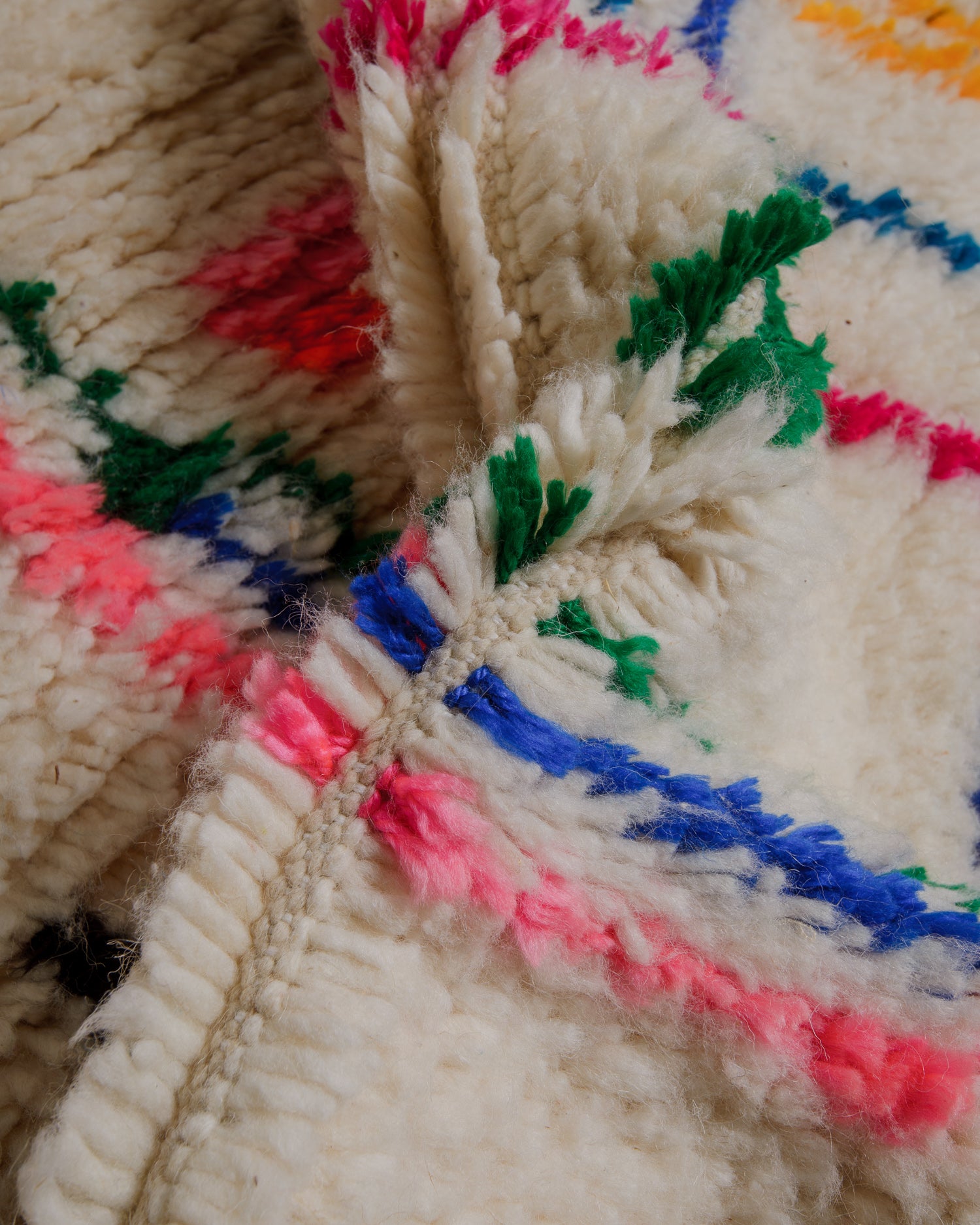 Close up of azilal rug with cream wool and pink, green and blue patterns.