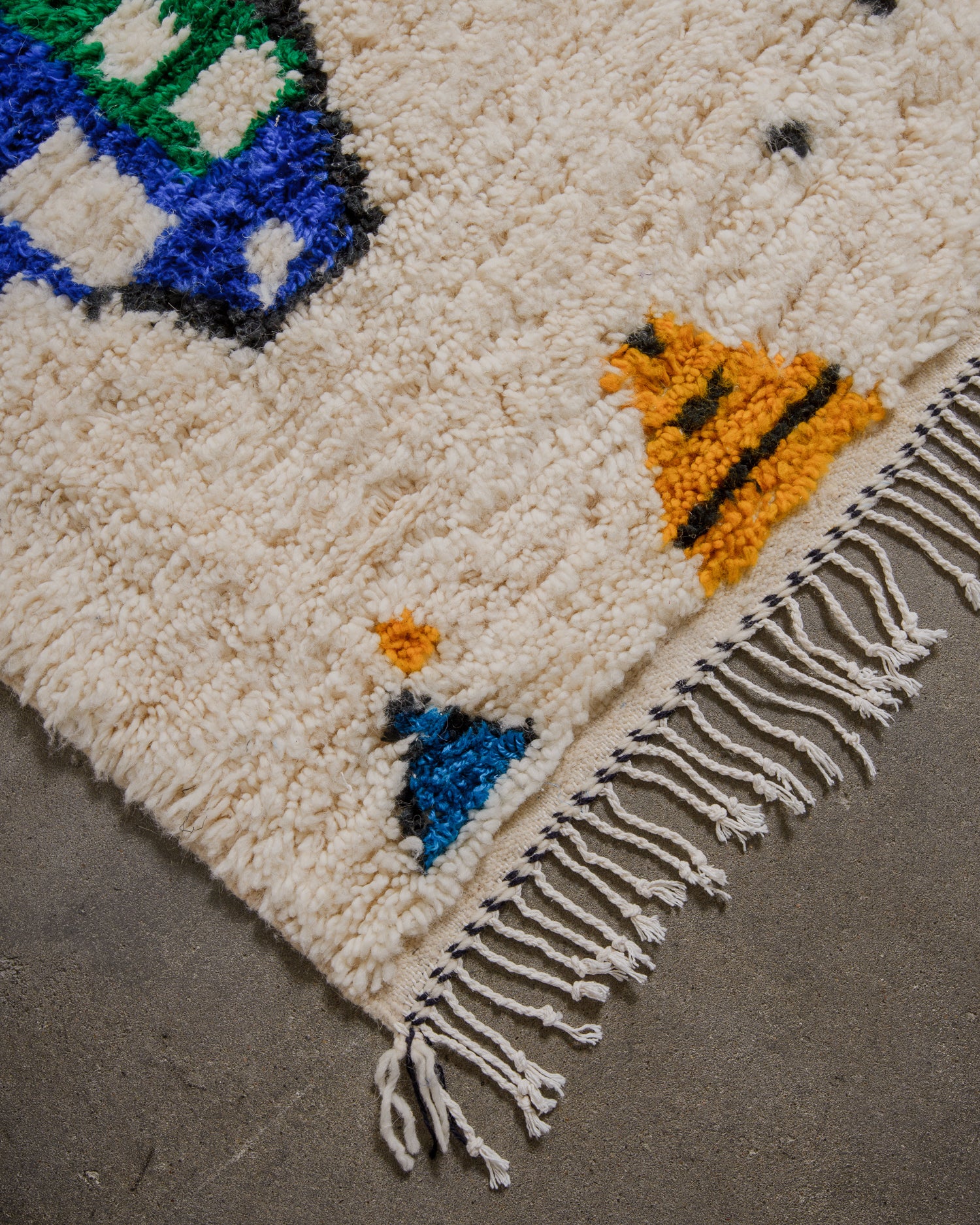 Corner of cream wool azilal rug with white cotton fringes. 
