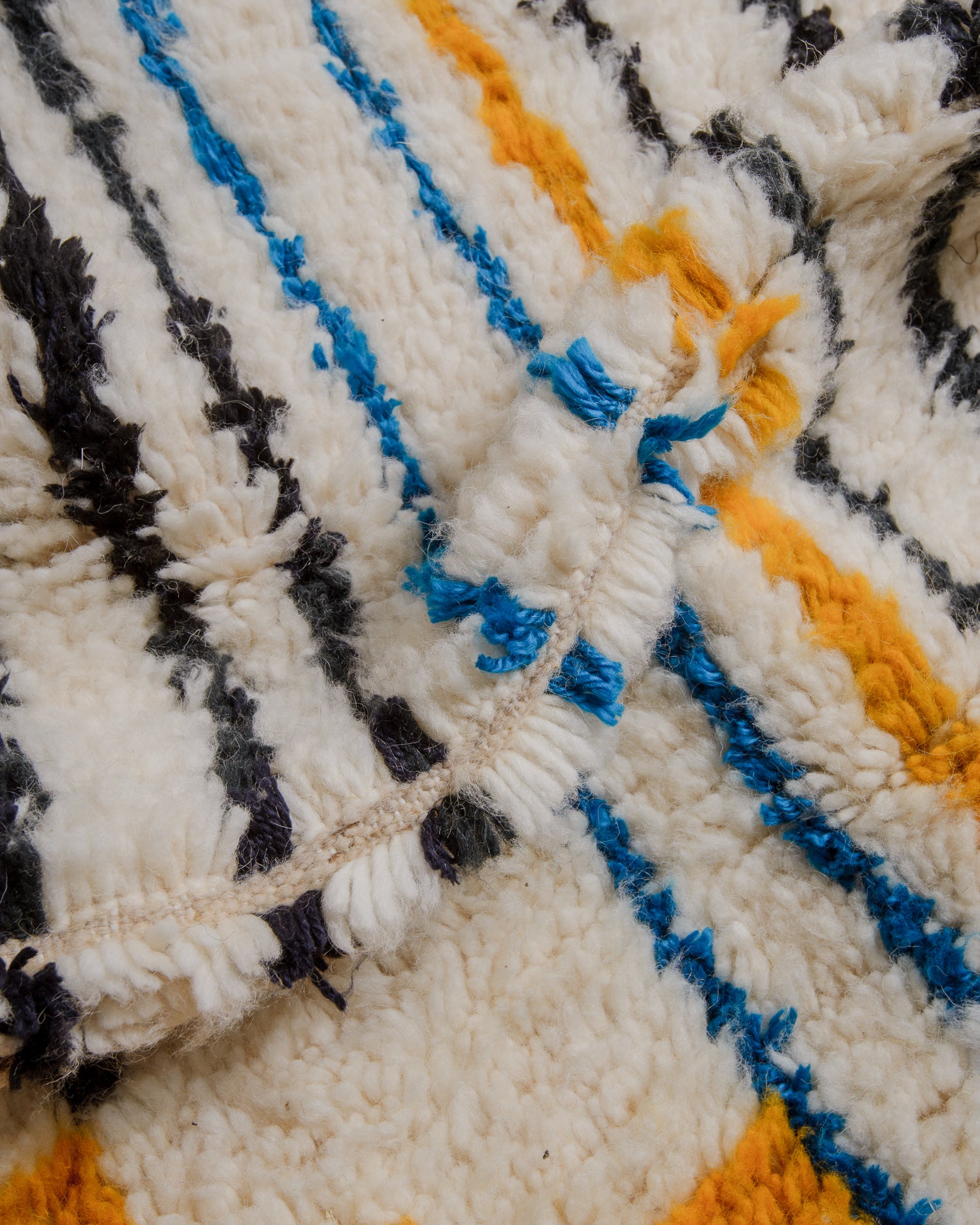 Close up of cream wool Azilal rug with black, blue and yellow stripes. 
