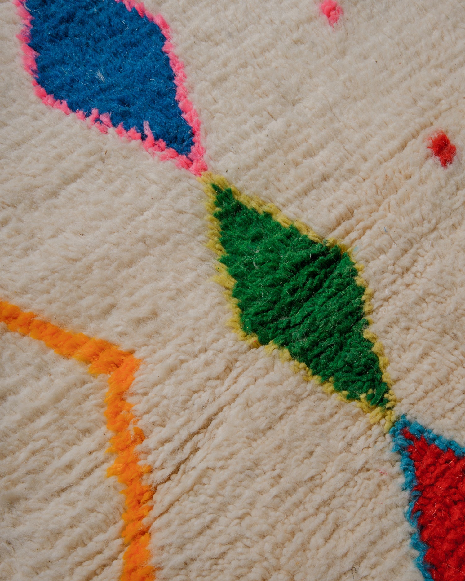 Detail or surface of cream azilal rug with diamond motifs in bright colour combinations. 