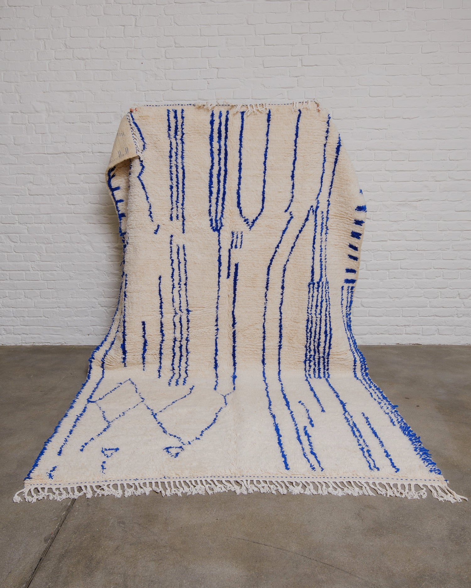 Cream azilal rug with abstract blue lines held in front of a white brick wall.