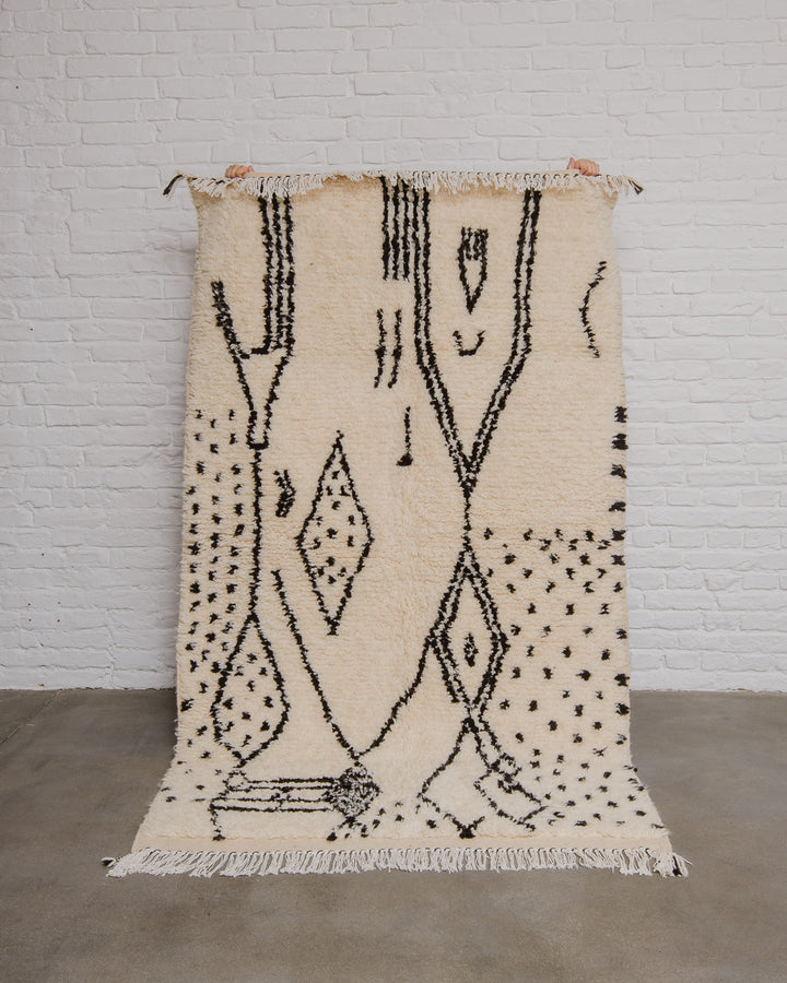 Cream and black patterned rug on a white brick wall background.