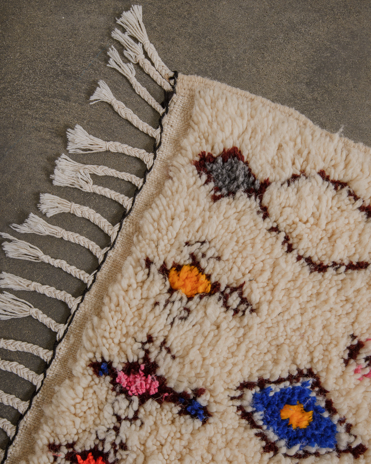 Corner of an azilal rug with white cotton tassels on a concrete floor. 