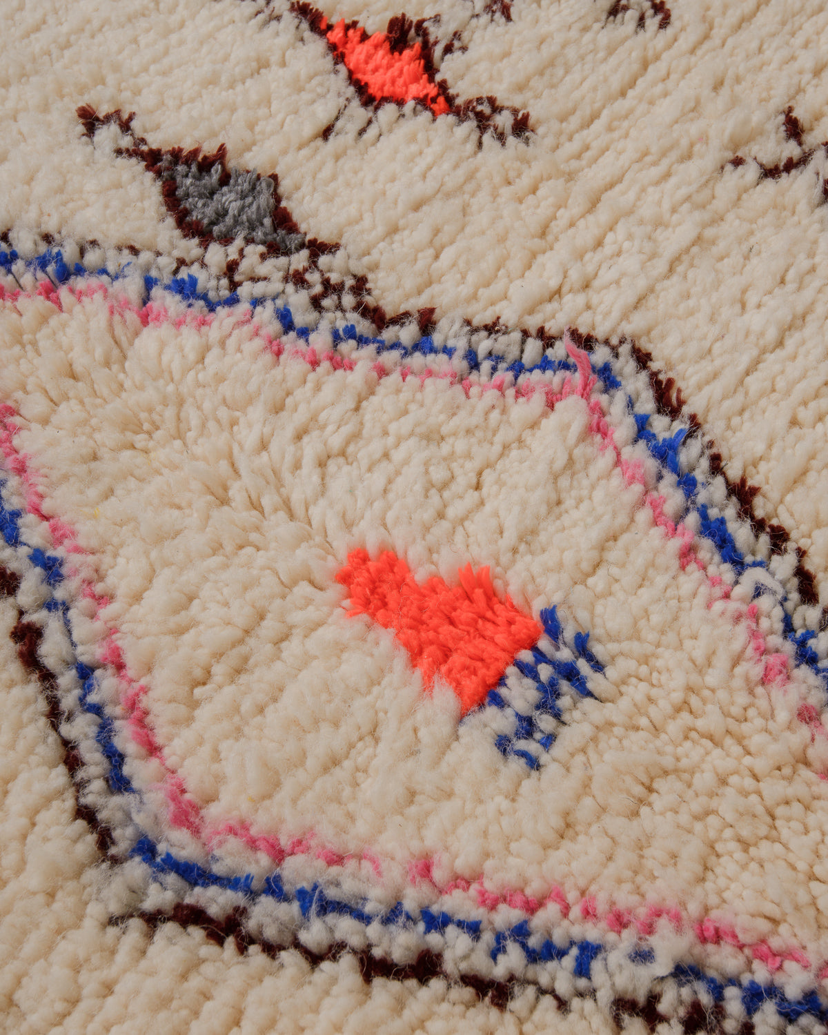 Close up of surface of cream wool rug with accents in blue, pink, brown and burgundy