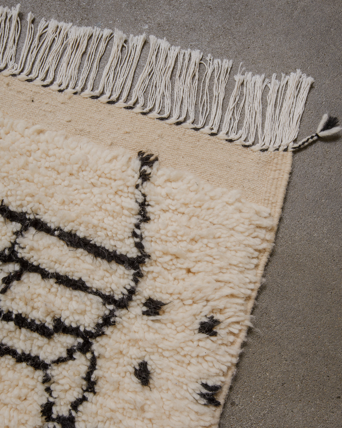 Close-up of a cream rug with black patterns and white fringe on a grey floor.