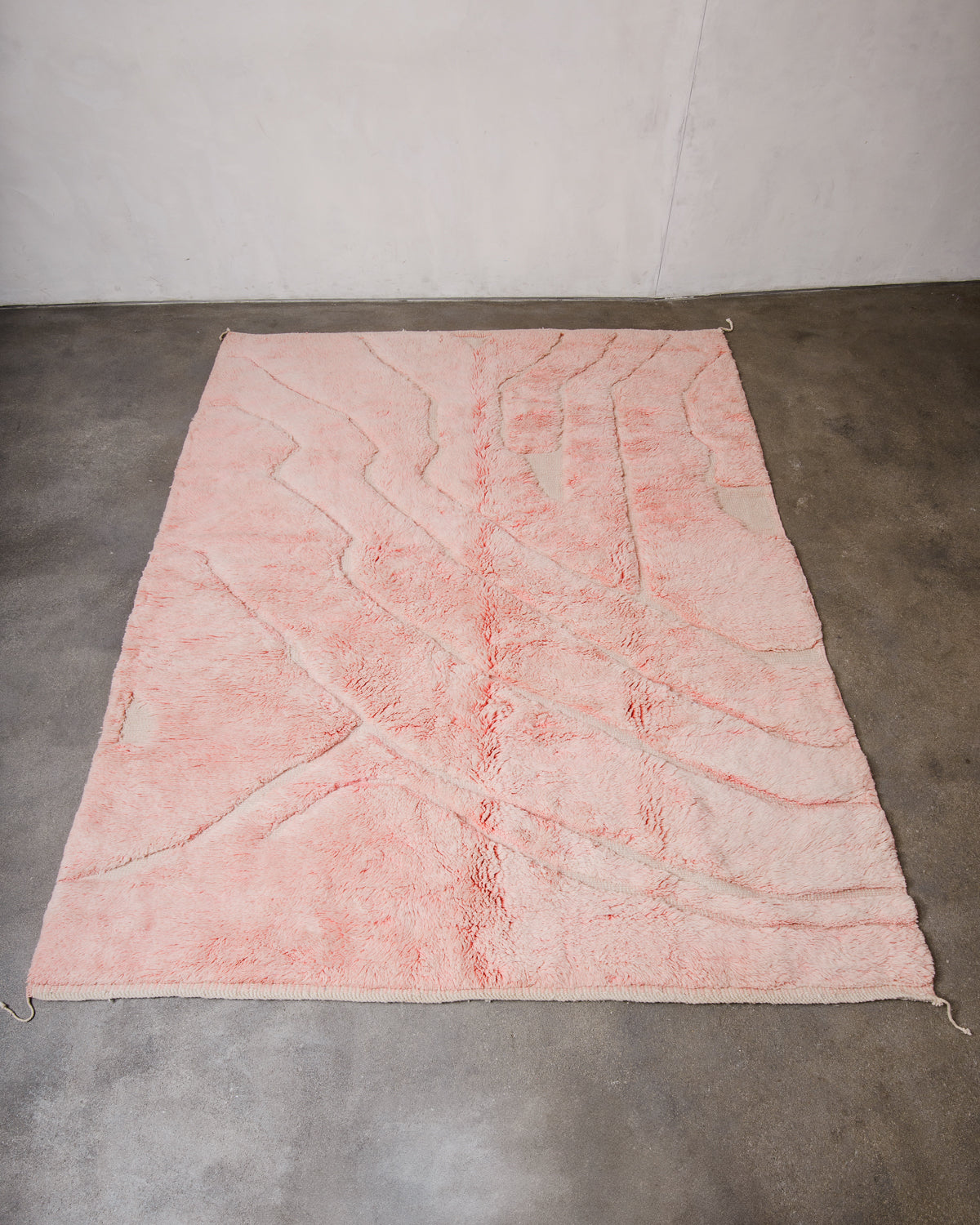 Berberlin Beni M'rirt Rug made of heavy wool pile in coral pink and cream laying flat on concrete floor. 
