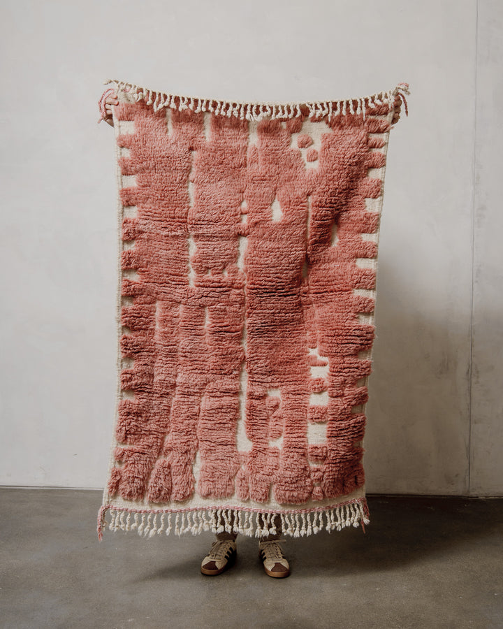 Rose and cream wool rug held up against a neutral background