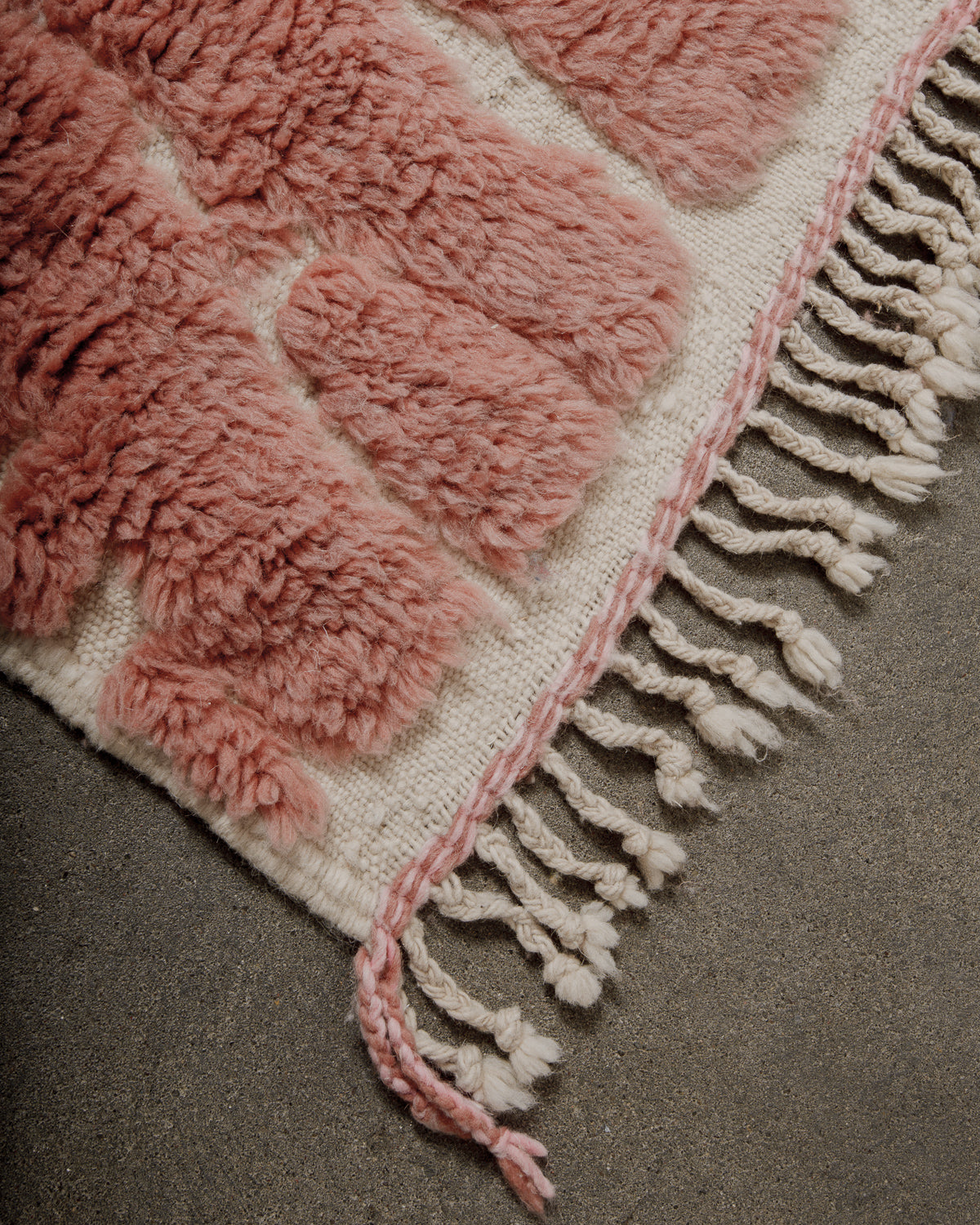 Close-up of a rose coloured rug with fringe on a neutral background
