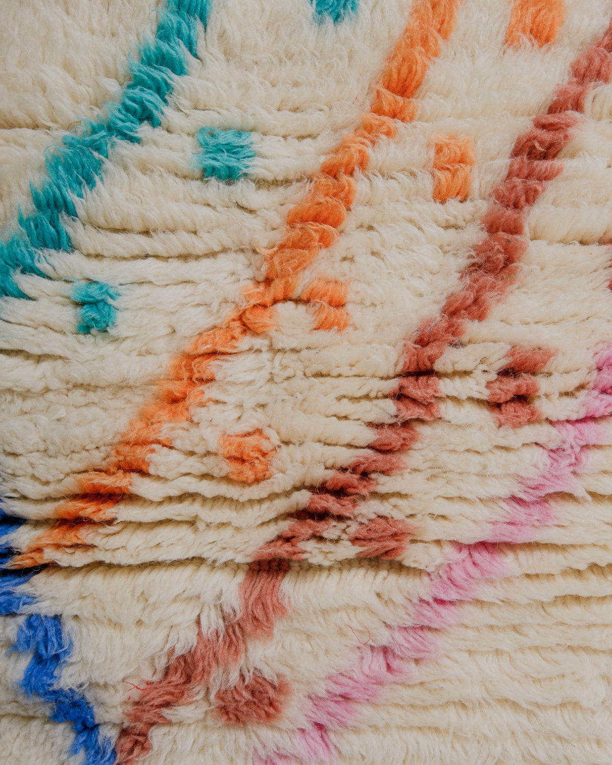 Close-up of a thick cream wool rug with green, blue and pink accents.
