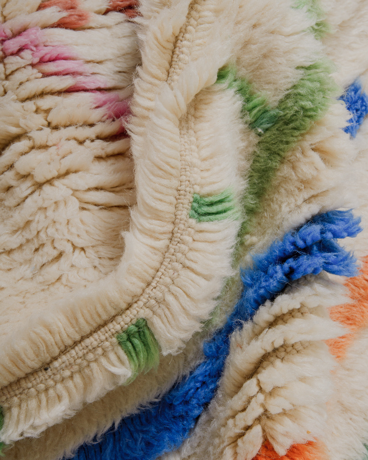 Close-up of a thick cream wool rug with green, blue and pink accents.