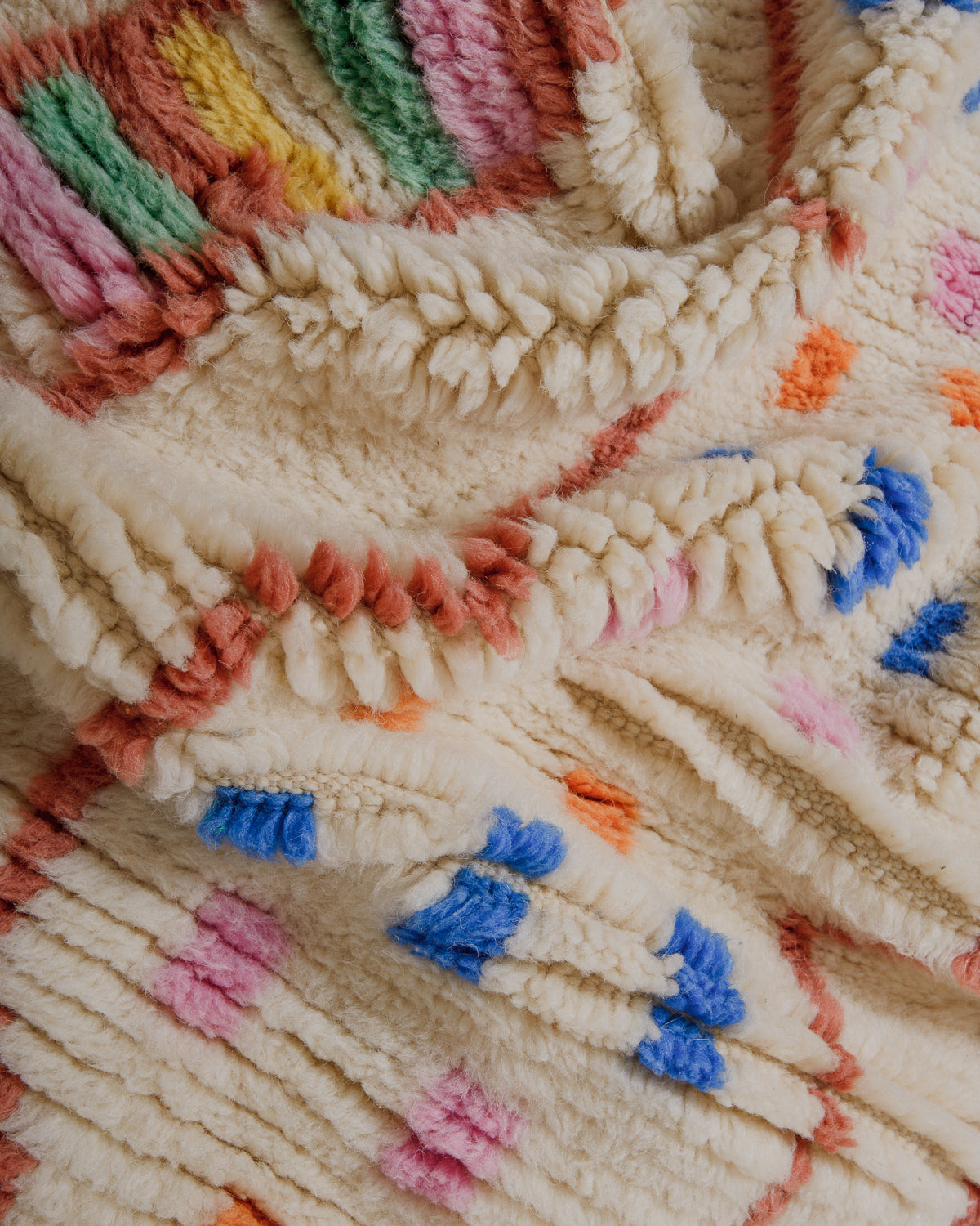Close-up of a fluffy wool rug made of cream, blue, pink, green and yellow wool.