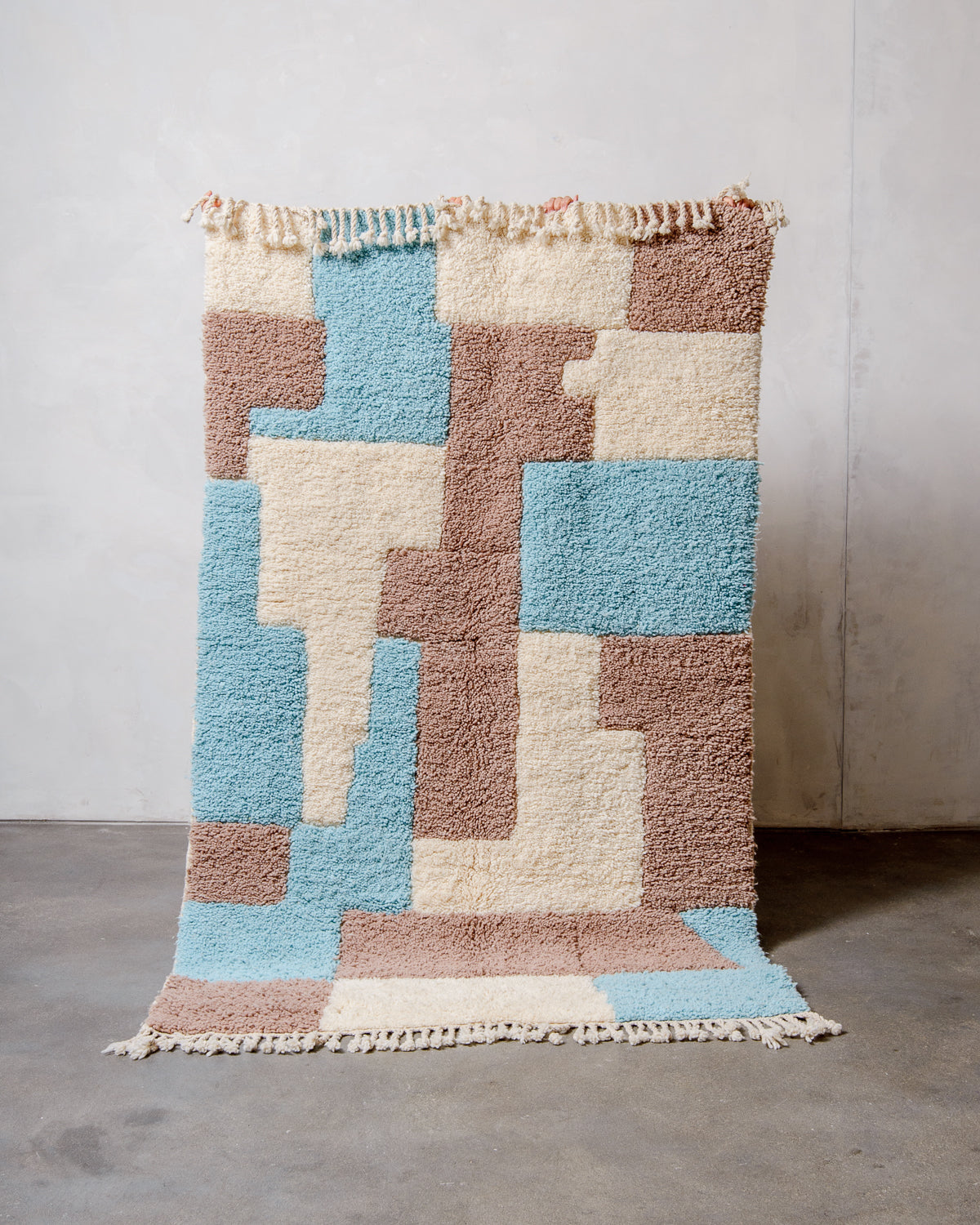 Berberlin Beniourain rug in colourful wool and cream, being held up in front of a white wall. 