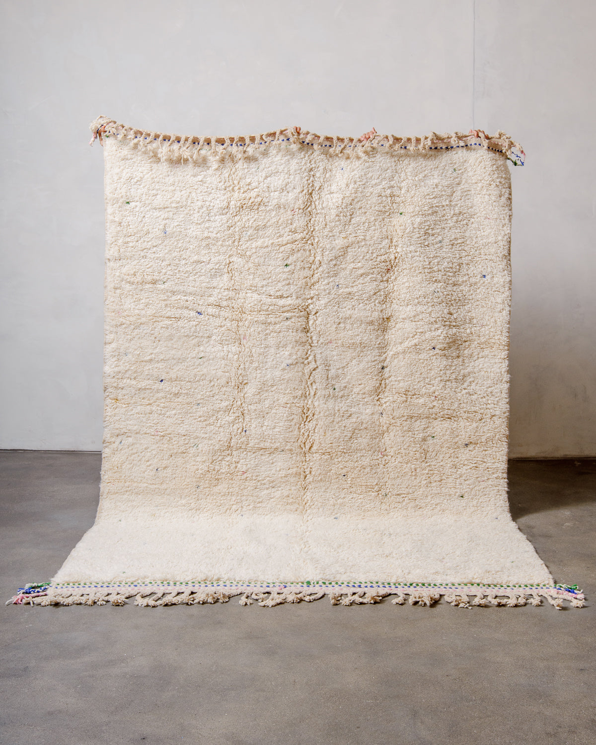 Berberlin Beniourain rug in cream wool with colourful dots being held up in front of a white wall. 