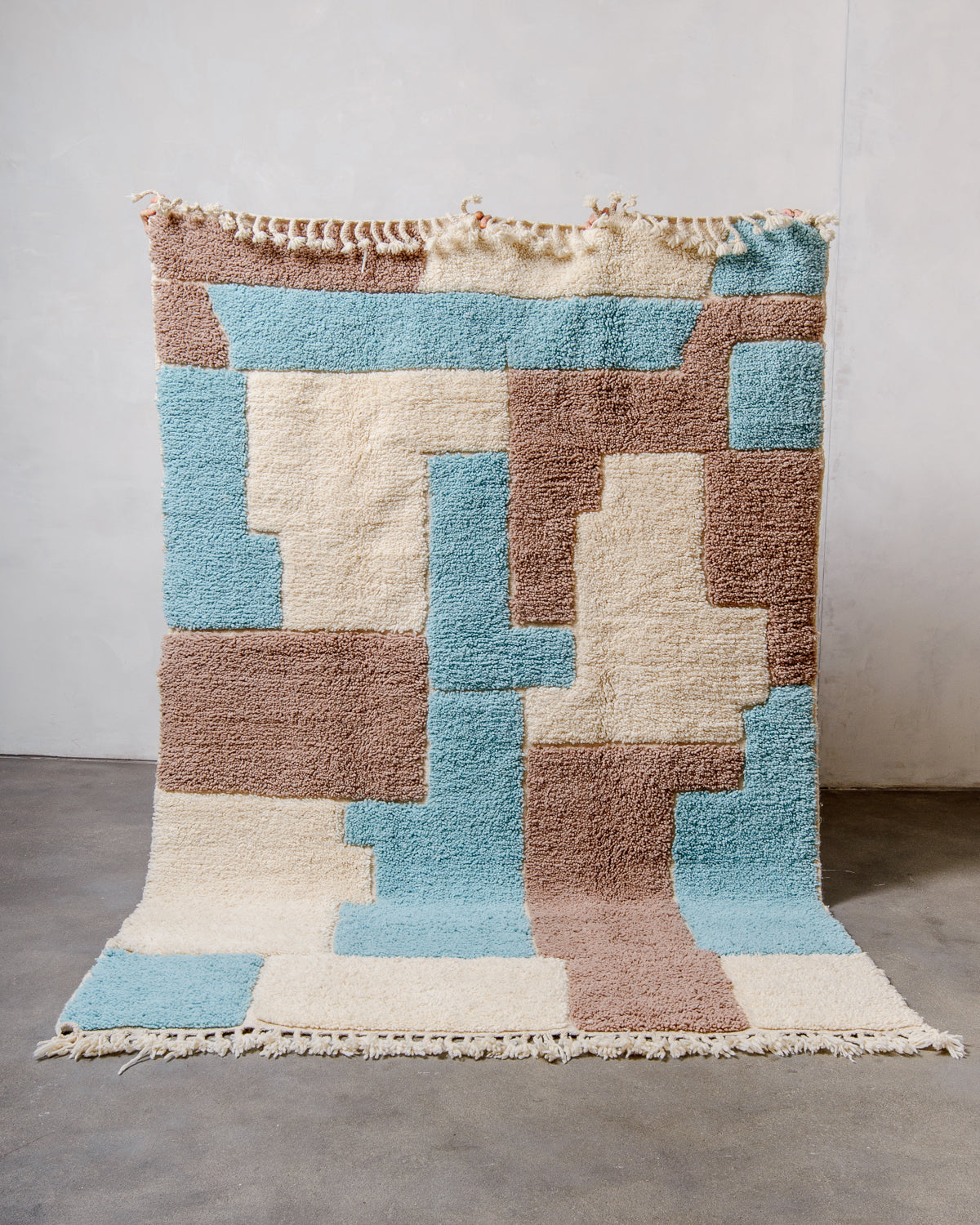 Berberlin Beniourain rug in colourful wool and cream, being held up in front of a white wall. 