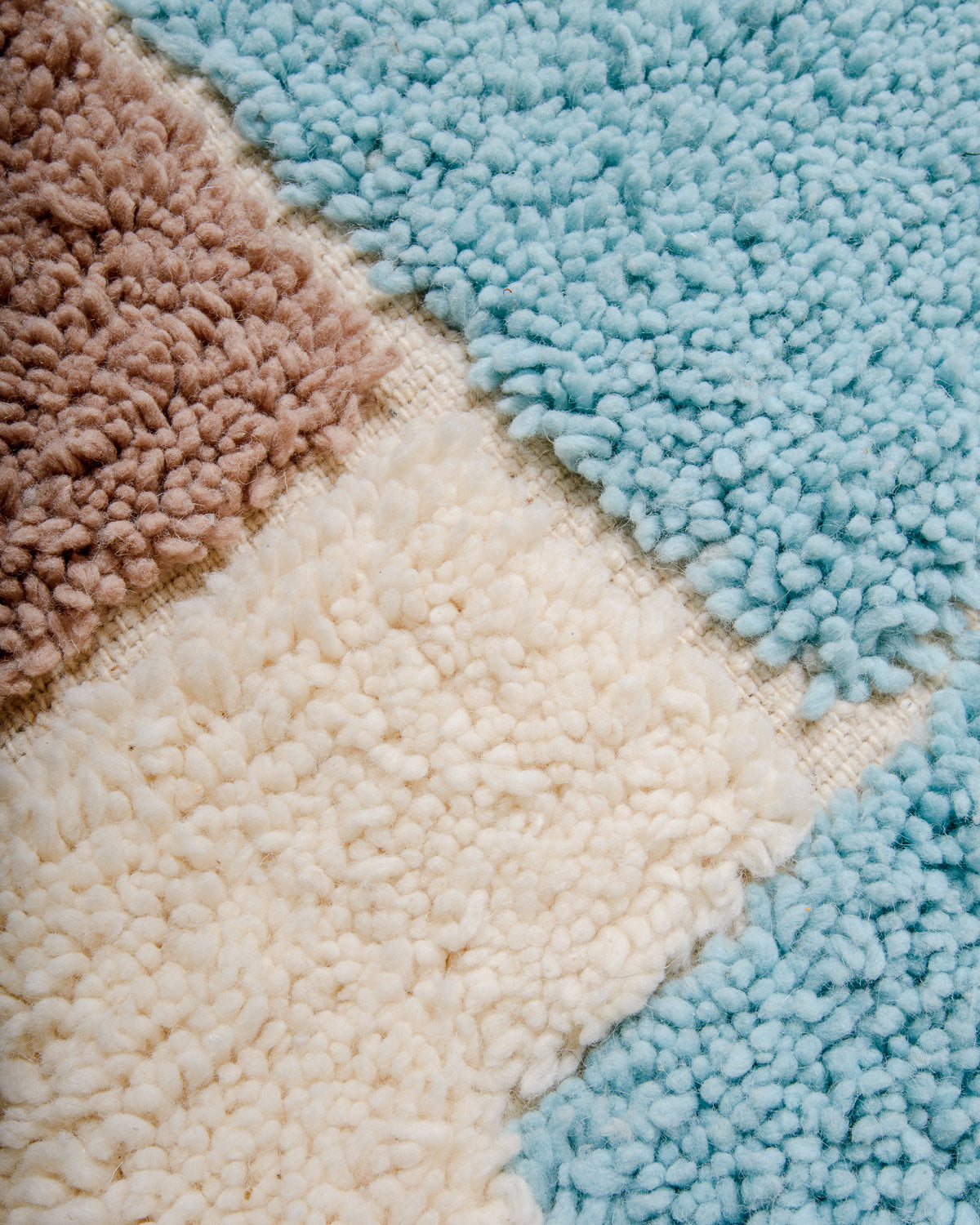 Close up of texture of Beniourain rug made of fluffy wool in cream, taupe brown and light sky blue.