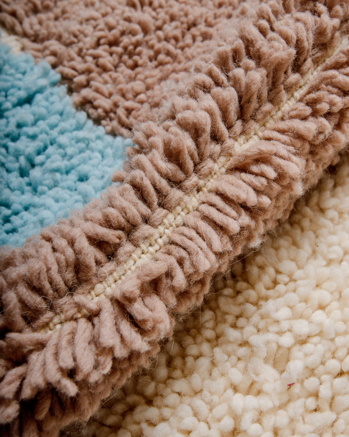 Close up of knots of Beniourain rug made of fluffy wool in cream, taupe brown and light sky blue.