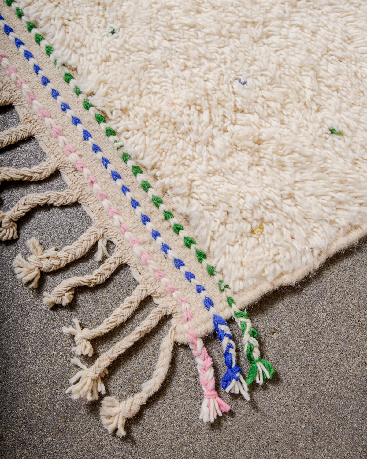 Corner of Berber rug with coloured weaving on the ends and natural wool tassels across the top. 