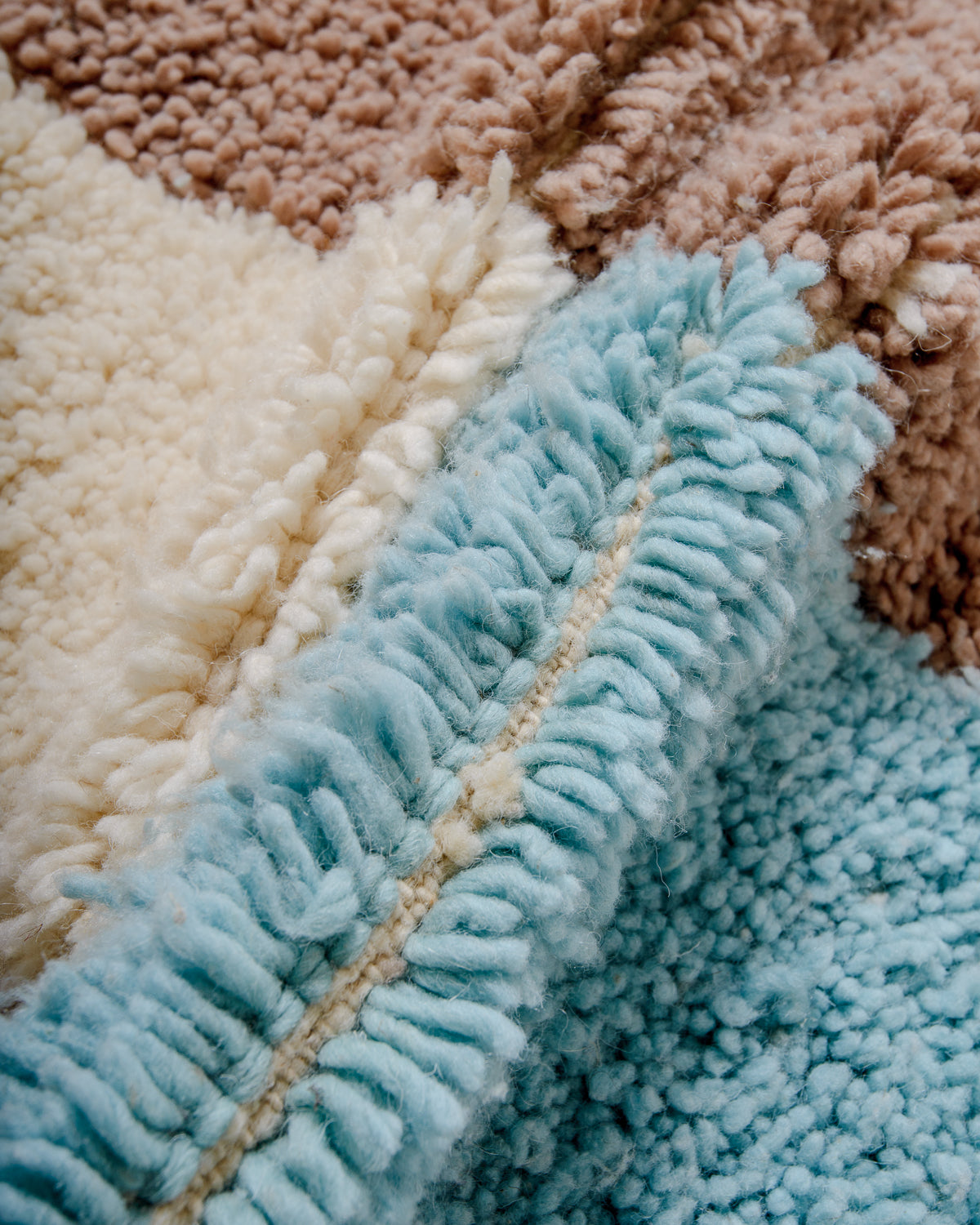 Close up of knots of Beniourain rug made of fluffy wool in cream, taupe brown and light sky blue.