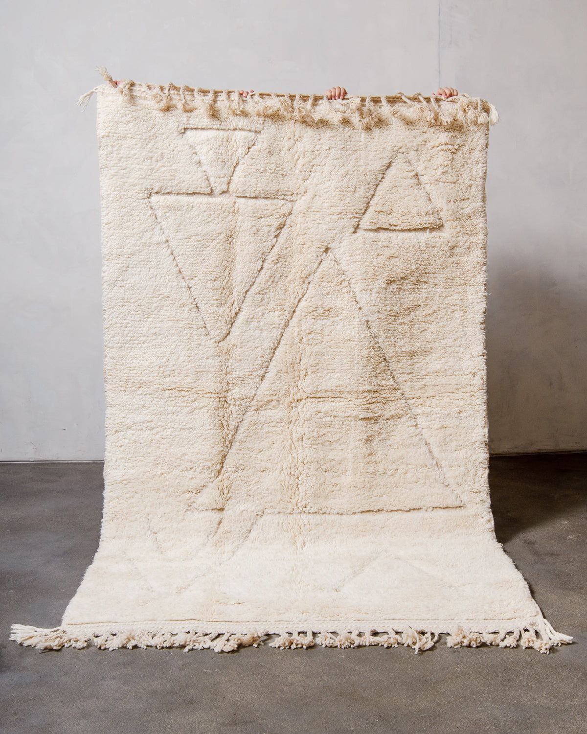 Berberlin Beniourain Rug made of cream wool being held up in front of a white wall. 