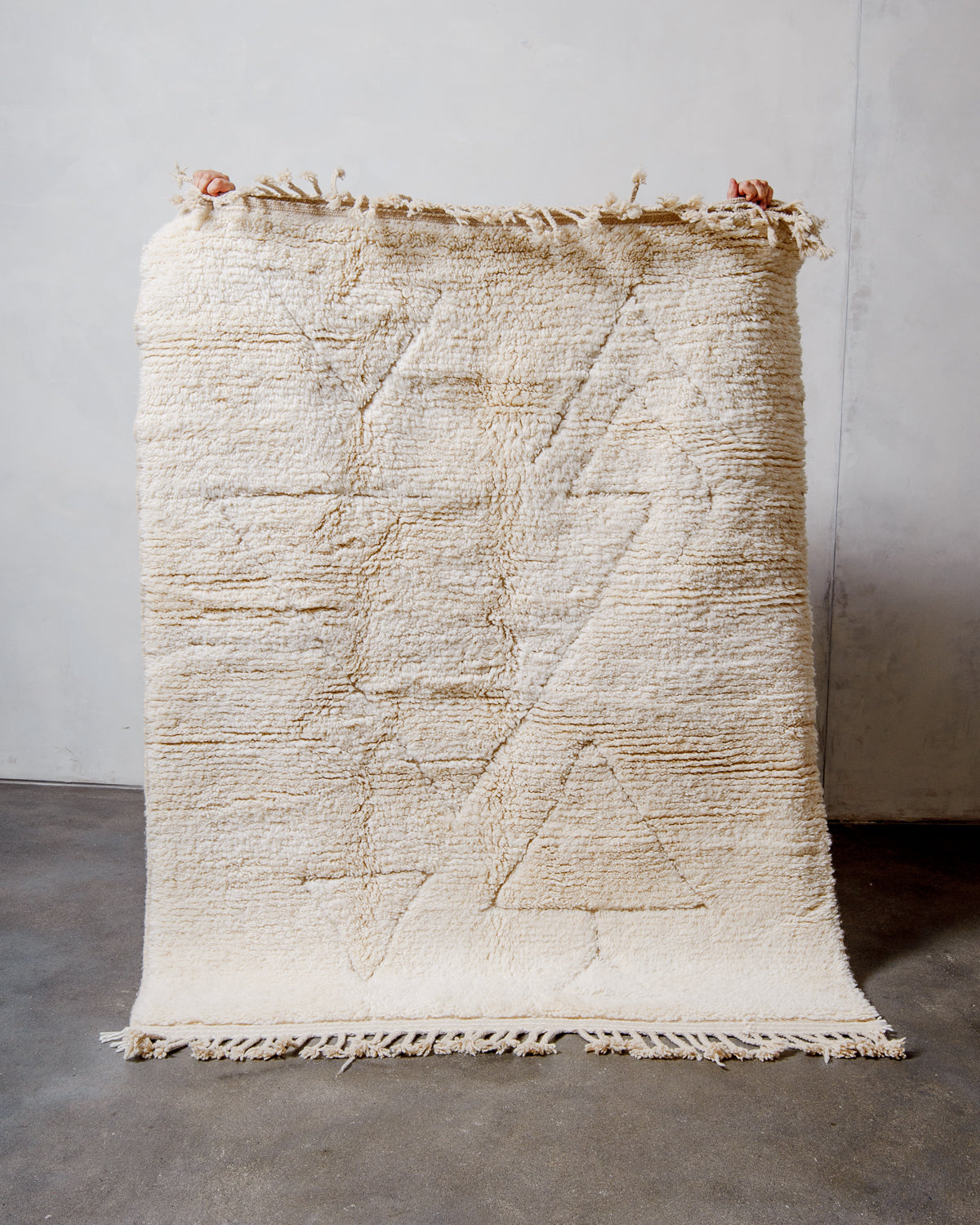 Berberlin Beniourain Rug made of cream wool being held up in front of a white wall. 